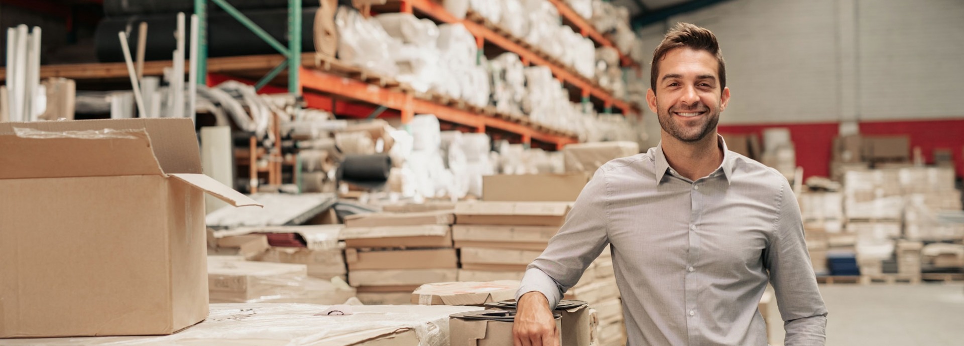 Manager glimlachend terwijl hij tegen de voorraad leunt in een groot magazijn