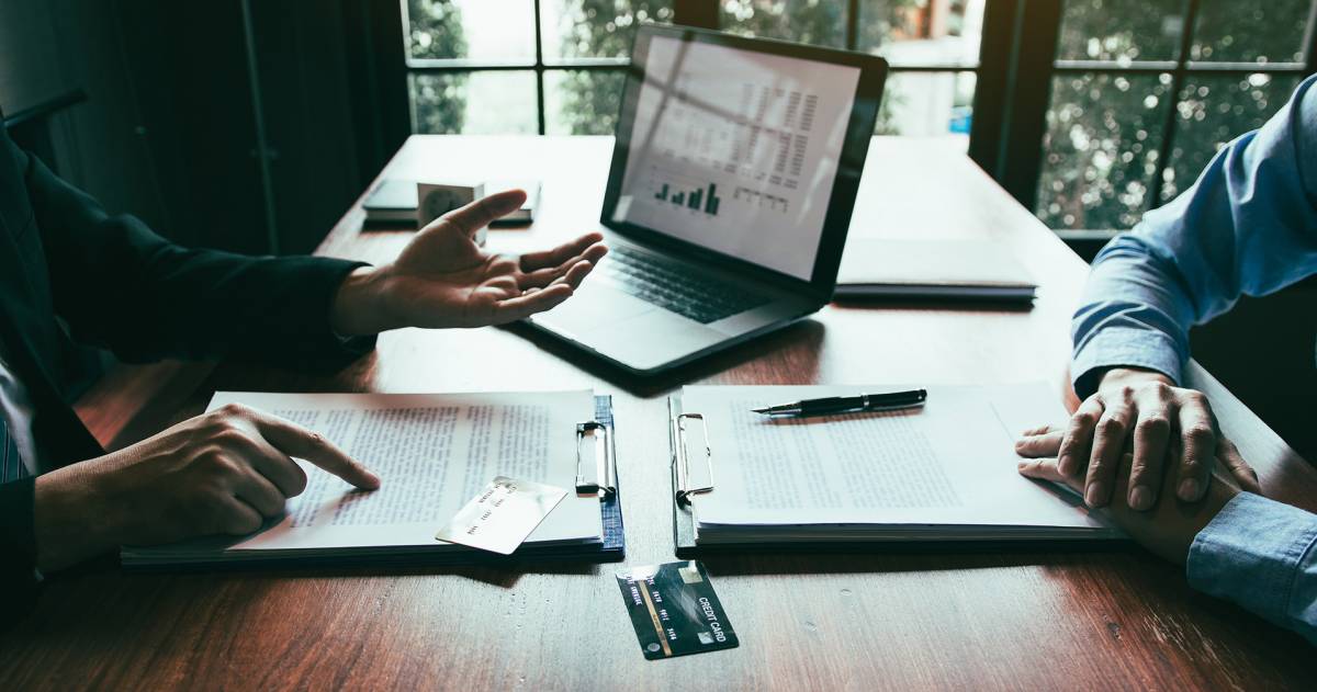 Klant bespreekt bij een medewerker van een bank zijn krediet mogelijkheden achter een bureau met papieren en een laptop